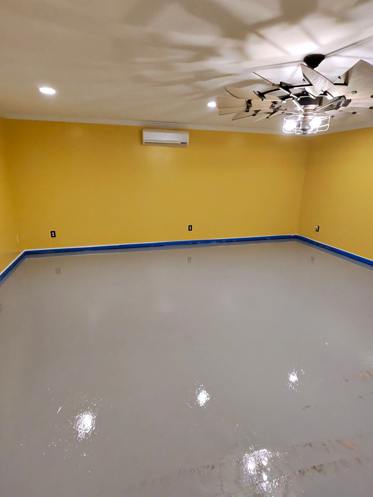 Gray primed floor with blue painter's tape along the walls